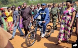 President Pierre Nkurunziza arrives riding a bicycle, accompanied by first lady Denise Bucumi Nkurunziza, right, to cast his vote for the presidential election, in Ngozi, Burundi, July 21, 2015.
