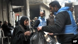 In this photo released by the Syrian official news agency SANA, a U.N relief worker, right, gives aid supplies to a Palestinian woman, at the gate of the besieged Yarmouk refugee camp, on the southern edge of the Syrian capital Damascus, Feb. 4, 2014.
