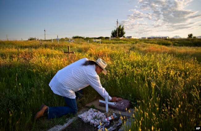 In this July 14, 2018, file photo, Kenny Still Smoking touches the tombstone of his 7-year-old daughter, Monica, who disappeared from school in 1979 and was found frozen on a mountain, as he visits her grave on the Blackfeet Indian Reservation in Browning