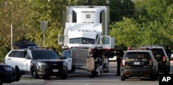 San Antonio police officers investigate the scene where immigrants were found dead in a tractor-trailer loaded outside a store in stifling summer heat, July 23, 2017, in San Antonio.
