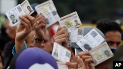 Venezuelan citizens hold up their identification cards for inspection by the Colombian immigration police, in Cucuta, Colombia, on the border with Venezuela, Feb. 22, 2018.