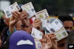 FILE - Venezuelan citizens hold up their identification cards for inspection by the Colombian immigration police, in Cucuta, Colombia, on the border with Venezuela, Feb. 22, 2018.