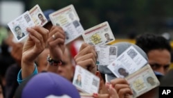 FILE - Venezuelan citizens hold up their identification cards for inspection by the Colombian immigration police, in Cucuta, Colombia, on the border with Venezuela, Feb. 22, 2018.