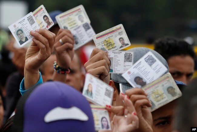 FILE - Venezuelan citizens hold up their identification cards for inspection by the Colombian immigration police, in Cucuta, Colombia, on the border with Venezuela, Feb. 22, 2018.