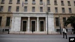 People walk past the Bank of Greece headquarters, in central Athens, March 27, 2015. 