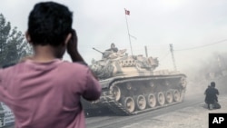 A boy looks at Turkish army tanks and armored personnel carriers moving toward the Syrian border, in Karkamis, Turkey, Aug. 25, 2016. 