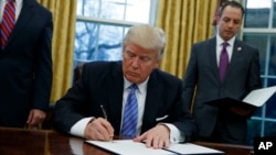 President Donald Trump signs an executive order to withdraw the U.S. from the 12-nation Trans-Pacific Partnership trade pact agreed to under the Obama administration, Jan. 23, 2017, in the Oval Office of the White House.