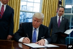 FILE - President Donald Trump signs an executive order to withdraw the U.S. from the 12-nation Trans-Pacific Partnership trade pact agreed to under the Obama administration, Jan. 23, 2017, in the Oval Office of the White House.