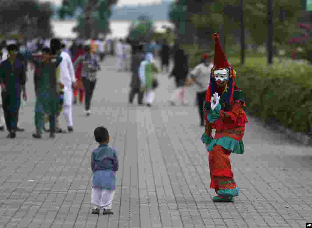 A clown looks at a child visiting Lake View park with his family on the outskirts of Islamabad, Pakistan.