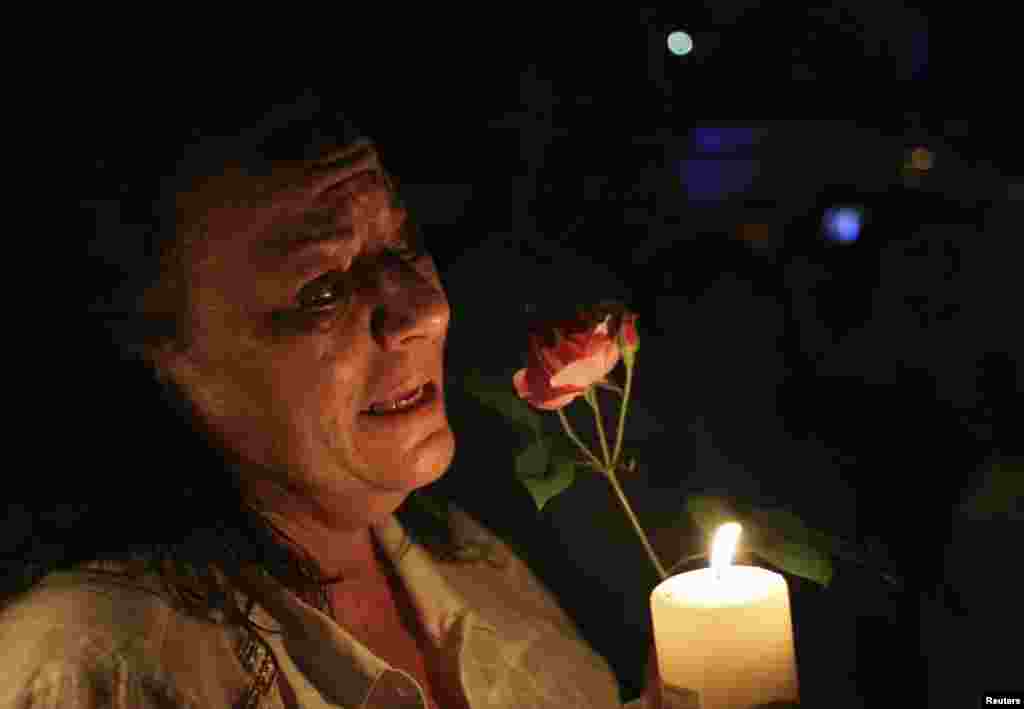 A women cries as she holds a candle and a flower outside former South African President Nelson Mandela's house in Houghton, Dec. 5, 2013.