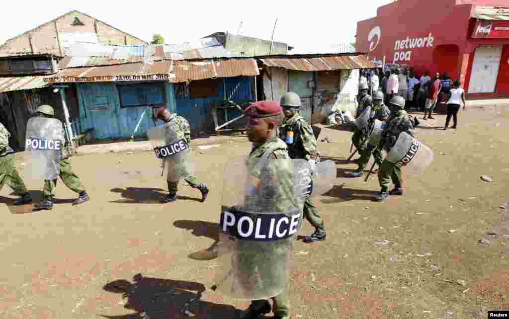 Riot police walk past residents in Nyallenda slums in Kenya's western town of Kisumu, 350km (218 miles) from the capital Nairobi as tension arises after Uhuru Kenyatta was declared winner of presidential election, Mar. 9, 2013.