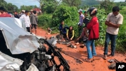 In this photo provided by Cambodia National Police, onlookers stand around the mangled wreckage of Cambodia's Prince Norodom Ranariddh's car after a collision with another vehicle outside Sihanoukville, Cambodia, Sunday, June 17, 2018. 