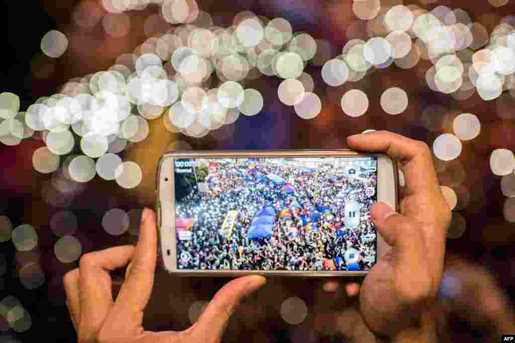 A pro-democracy protester photographs people waving lights next to the central government offices in Hong Kong. Activists, marking a month of mass protests, call for an evening rally and wear masks to ward off police tear gas.