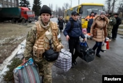 FILE - A member of the Ukrainian armed forces assists local residents onto a bus to flee the military conflict, in Debaltseve, eastern Ukraine, Feb. 6, 2015.