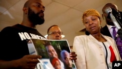 Lesley McSpadden, right, the mother of 18-year-old Michael Brown, watches as Brown's father, Michael Brown Sr., holds up a family picture of himself, his son, (top left) and a young child during a news conference, Aug. 11, 2014, in Ferguson, Mo.