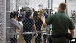In this photo provided by U.S. Customs and Border Protection, a U.S. Border Patrol agent watches as people who've been taken into custody related to cases of illegal entry into the United States, stand in line at a facility in McAllen, Texas.
