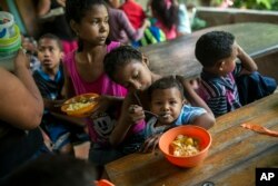 Franyelis, 8, feeds her baby brother Joneiber as their mother, Francibel Contreras, holds a bowl of scrambled eggs and rice, at a soup kitchen in the Petare slum, Caracas, Venezuela, Feb. 14, 2019.