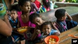 Franyelis (8), menyuapi adiknya yang masih bayi, Joneiber sementara ibu mereka Francibel Contreras memegang semangkok nasi dan telur di daerah kumuh Petare, Caracas, Venezuela, 14 Februari 2019 . (Foto: dok).