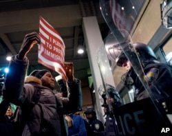 FILE - A protester stands facing police officers at an entrance of Terminal 4 at John F. Kennedy International Airport in New York, Jan. 28, 2017, after earlier in the day two Iraqi refugees were detained while trying to enter the country.