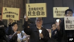 A protester, center, holds up a placard reading: 'Supporting Wukan villagers, democracy autonomy' during a candlelight vigil outside the China Liaison Office in Hong Kong to support the Wukan villagers, December 20, 2011.