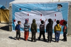 Displaced Syrian children read a poster, outlining 7 steps to prevent the spread of COVID-19 coronavirus disease, at a camp for the internally displaced near Dayr Ballut, near the Turkish border.