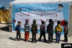 Displaced Syrian children read a poster, outlining 7 steps to prevent the spread of COVID-19 coronavirus disease, at a camp for the internally displaced near Dayr Ballut, near the Turkish border.