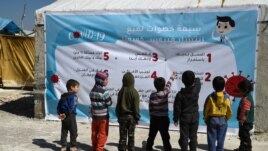Displaced Syrian children read a poster, outlining 7 steps to prevent the spread of COVID-19 coronavirus disease, at a camp for the internally displaced near Dayr Ballut, near the Turkish border.