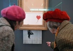 People look at the shredded Banksy painting "Love is in the Bin' at the Museum Frieder Burda in Baden-Baden Tuesday, Feb. 5, 2019, where the work will be shown from Feb. 5 to March 3, 2019.