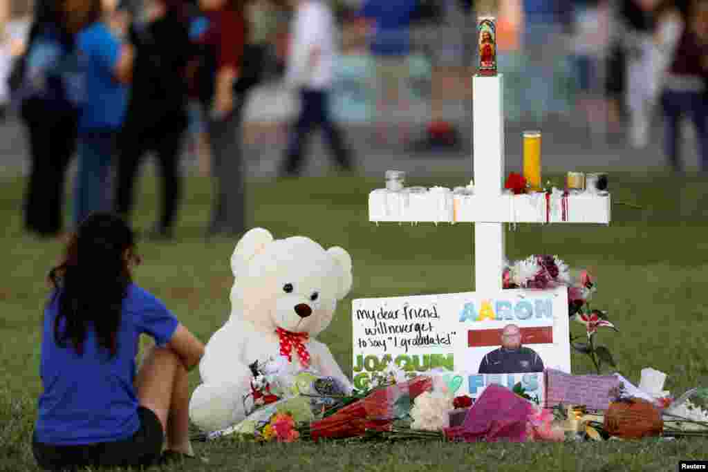 A mourner sits by a cross adorned with pictures of victims, along with flowers and other mementoes, at a memorial two days after the shooting at Marjory Stoneman Douglas High School in Parkland, Florida, Feb. 16, 2018.
