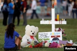 FILE - A mourner sits by a cross adorned with pictures of victims, along with flowers and other mementos, at a memorial two days after the shooting at Marjory Stoneman Douglas High School in Parkland, Florida, Feb. 16, 2018.