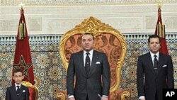 In this photo released by the Royal Palace, Morocco's King Mohamed VI flanked by his son Moulay El Hassan, left ,and his Brother Prince Moulay Rachid, right , listens to the national anthem after he delivered a speech to the nation, March, 9, 2011, at the