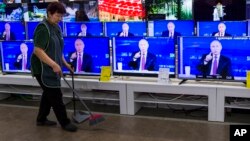 A cleaner walks past a store in Moscow with TV sets showing Russian President Vladimir Putin during his annual live call-in show, June 15, 2017.