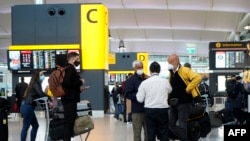 Wisatawan yang memakai masker wajah karena pandemi Covid-19, berdiri di meja check-in di Terminal 2 Bandara Heathrow di London barat pada 21 Desember 2020. (Foto: AFP)