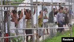 FILE - Asylum-seekers look through a fence at the Manus Island detention center in Papua New Guinea, March 21, 2014. 