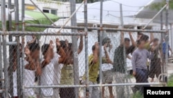 FILE - Asylum-seekers look through a fence at the Manus Island detention center in Papua New Guinea, March 21, 2014. 