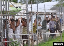 FILE - Asylum-seekers look through a fence at the Manus Island detention center in Papua New Guinea, March 21, 2014.
