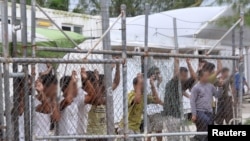 FILE - Asylum-seekers look through a fence at the Manus Island detention center in Papua New Guinea, March 21, 2014. 