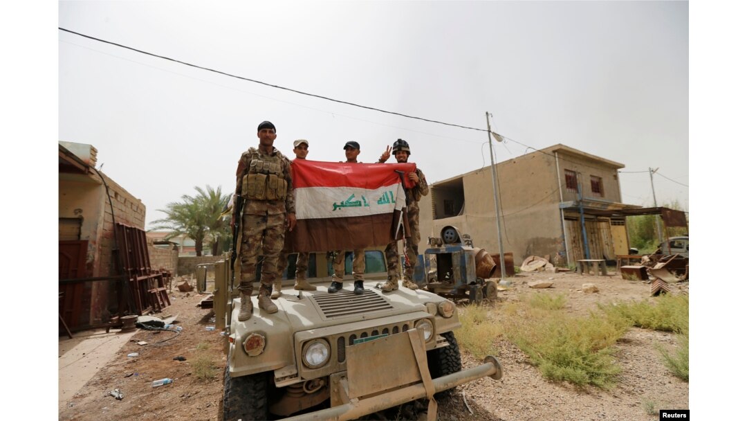 Iraqi army soldiers hold Iraqi flag on a top of a military vehicle in the centre of Fallujah, Iraq, June 18, 2016.
