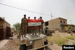 Iraqi army soldiers hold Iraqi flag on a top of a military vehicle in the centre of Fallujah, Iraq, June 18, 2016.