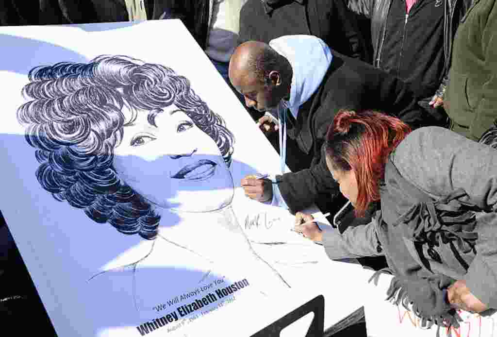 Para penggemar menulis di sebuah poster bergambarkan Whitney Houston dekat lokasi upacara penghormatan terakhir bagi Houston di Gereja New Hope Baptist di Newark, New Jersey, 18 Februari 2012 (AP).