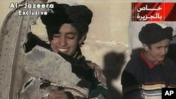 In this image made from a video broadcast by Al-Jazeera, Nov. 7, 2001, a young boy, left, identified as Hamza bin Laden holds what the Taliban says is a piece of U.S. helicopter wreckage.