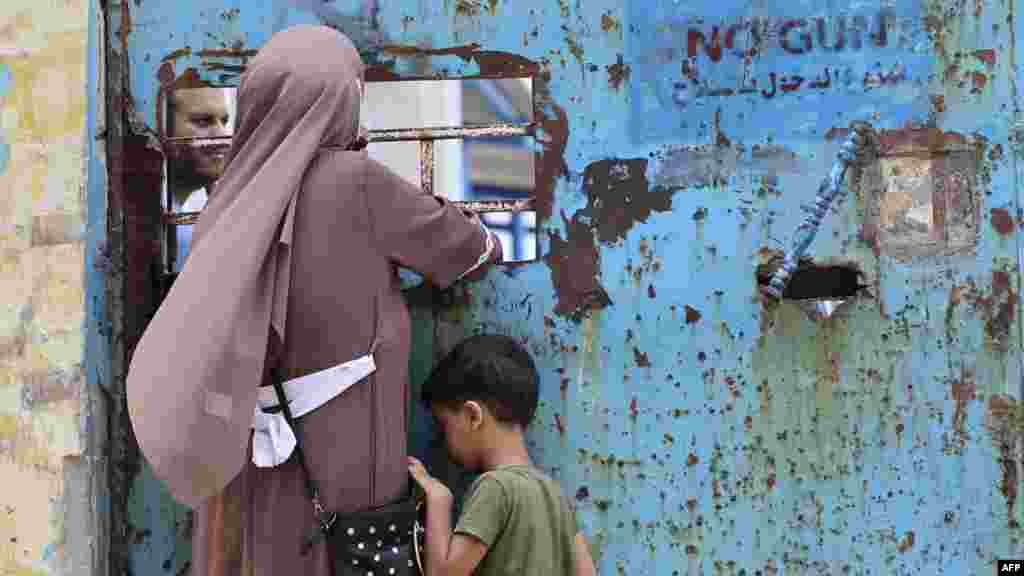 Palestinka i njen sin stoje ispred prozora centra za distribuciju humanitarne pomoći kojim rukovodi Agencija UN za pomoć palestinskim izbeglicama (UNRWA) u gradu Gazi (Foto: AFP/ Mohammed Abed)
