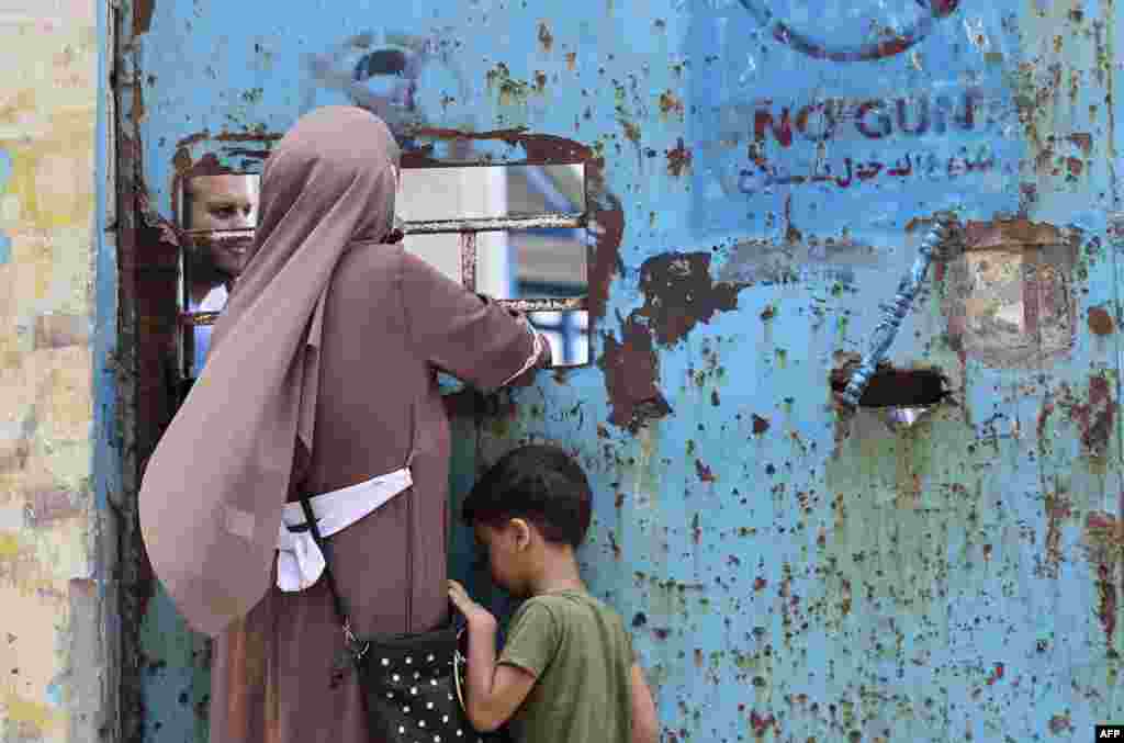 A Palestinian woman and her child stand next to a window of an aid distribution center run by the United Nations Relief and Works Agency (UNRWA) in Gaza City.