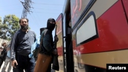 A masked rebel fighter boards a bus with his weapon as rebel fighters and their families evacuate the besieged Waer district in the central Syrian city of Homs, May 21, 2017. 