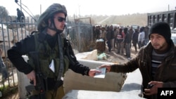 A member of the Israeli security forces hands a Palestinian worker his ID upon his transport out of the Tekoa settlement south of Jerusalem on Jan. 18, 2016, after Israeli authorities denied them entry following a stabbing attack.
