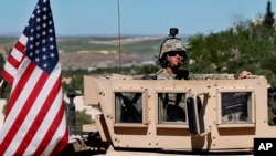 FILE - In this April 4, 2018 file photo, a U.S. soldier sits on his armored vehicle on a road leading to the front line in Manbij, Syria.