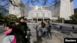 People walk past the headquarters of the People's Bank of China as two police officials patrol the area in Beijing Nov. 20, 2013. 