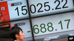 Seorang perempuan melewati papan elektronik menunjukkan posisi indeks saham acuan Japan Nikkei 225 di Tokyo, Jumat (12/2).