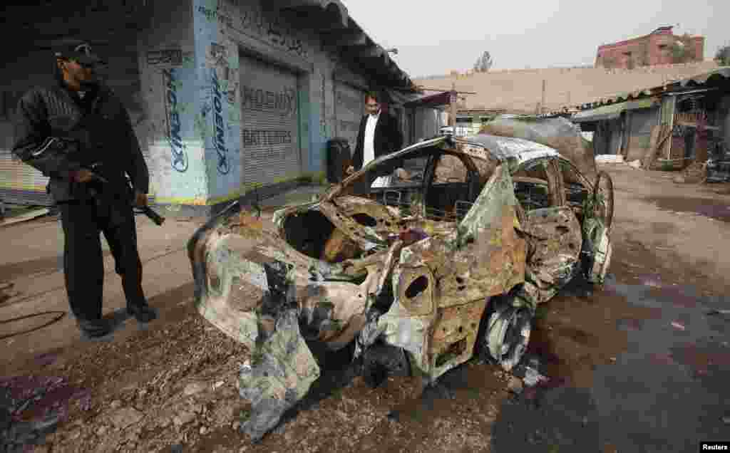 A police officer stands near a car which was damaged during a bomb attack at Fauji Market in Peshawar December 17, 2012. The blast in the market in northwest Pakistan on Monday killed at least 15 people, a security official said. The official said at leas