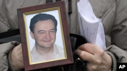 FILE - A portrait of Sergei Magnitsky, who died in jail, is held by his mother Nataliya Magnitskaya, in Moscow, Nov. 30, 2009. 